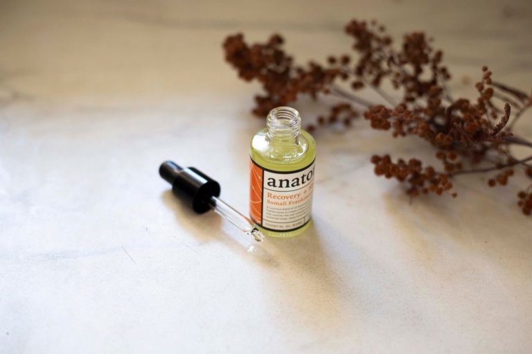 Anatome serum bottle with dropper on a light surface with dried flowers.