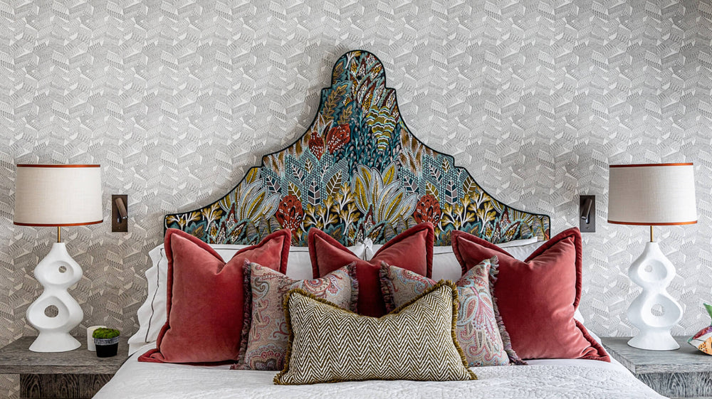Claudia savoir headboard with colourful patterns and pillows on a bed against a patterned wallpaper.