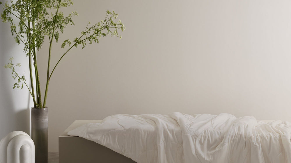 Minimalist bedroom with a bed, A duvet laid out on a shelf, and a vase of plants on a neutral background