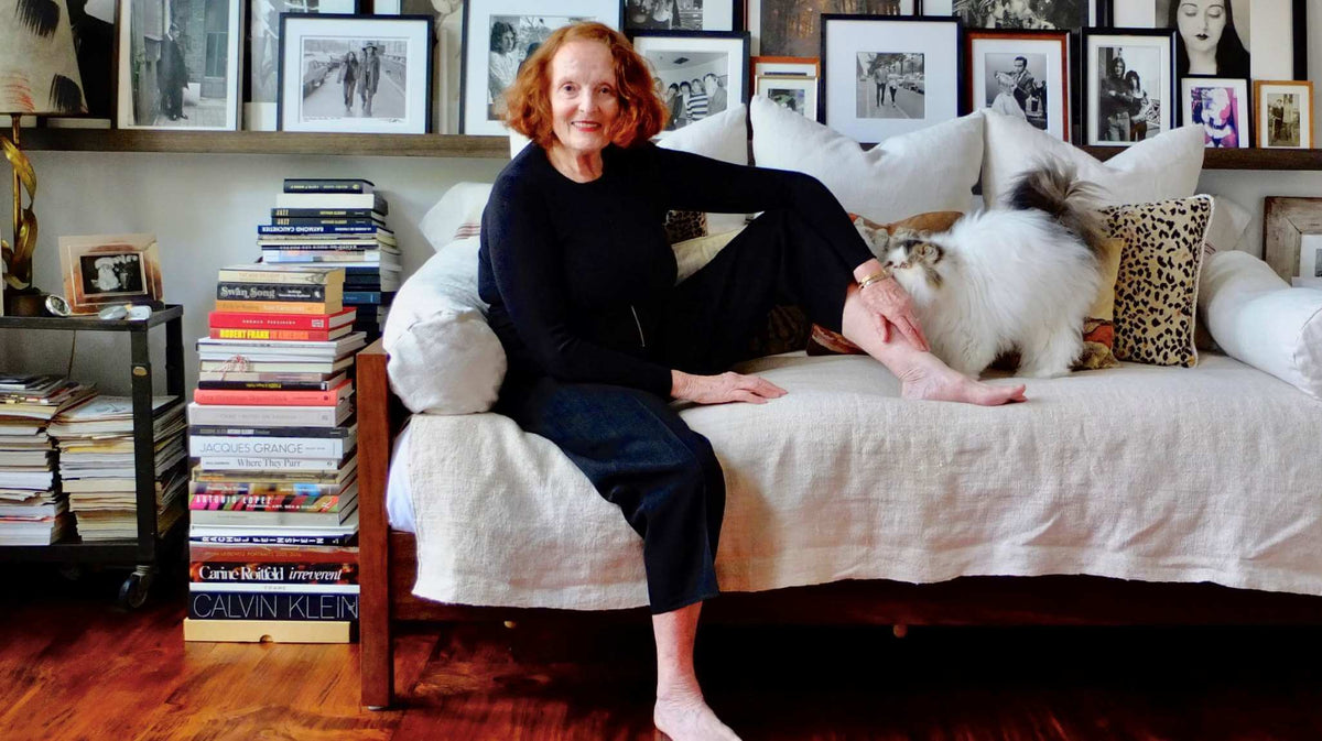 Grace Coddington sitting on a couch with a cat, surrounded by books and framed pictures.