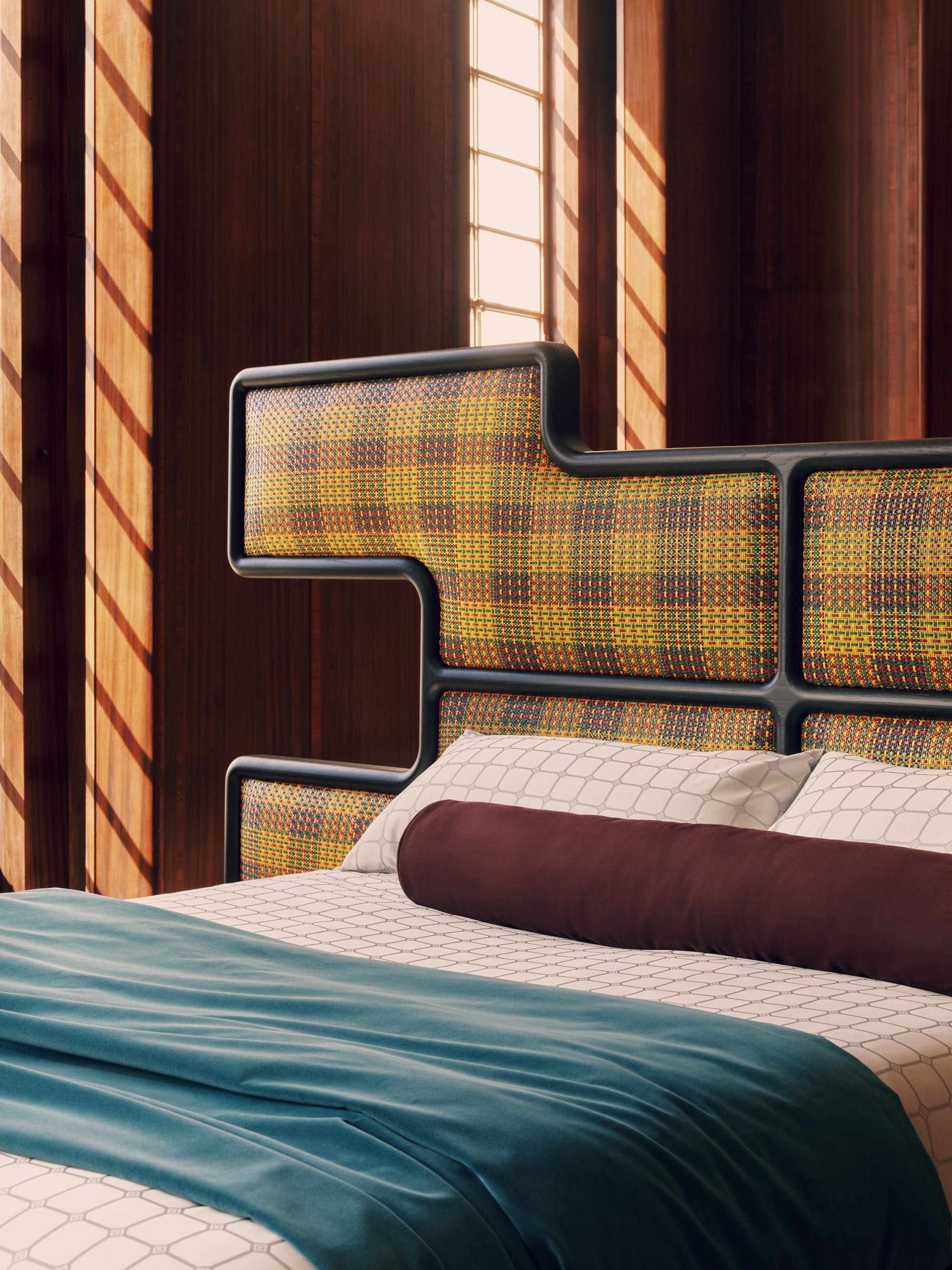 Modern bed with a checked headboard in a room with wooden walls and a window.