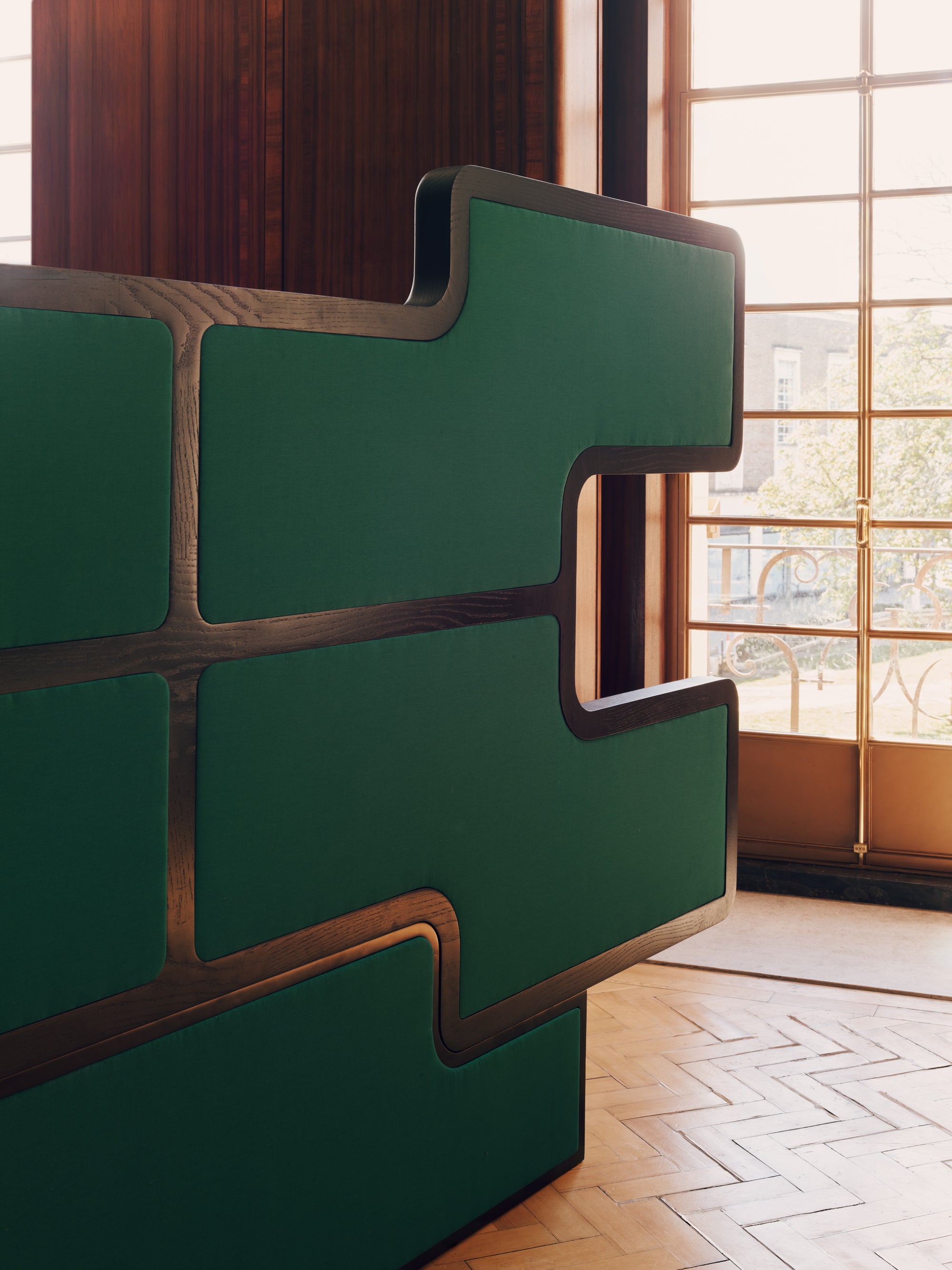 Green and brown geometric back headboard in a room with large windows.