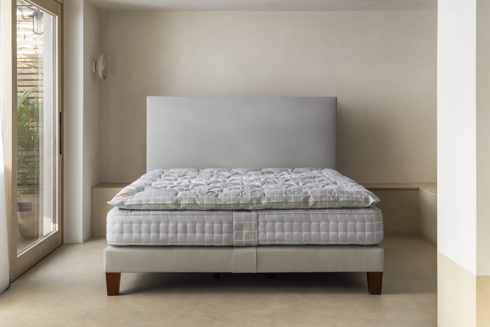 Mattress and topper on a grey upholstered bed frame in a minimalistic bedroom setting