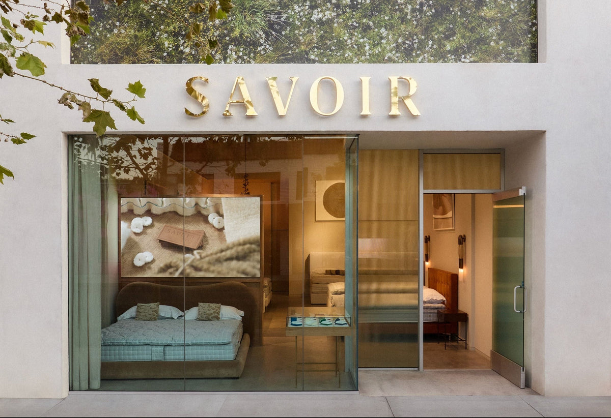 Savoir showroom storefront with a large green forest-patterned wall mural and gold SAVOIR lettering above glass windows.