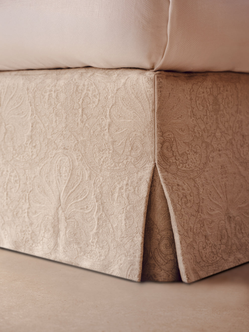 Close-up of the beige upholstered Stella bed valence with a subtle jacquard weaving, shown next to a pillow on a bed.