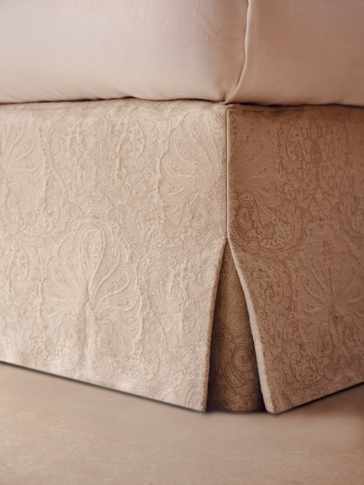 Close-up of the beige upholstered Stella bed valence with a subtle jacquard weaving, shown next to a pillow on a bed.