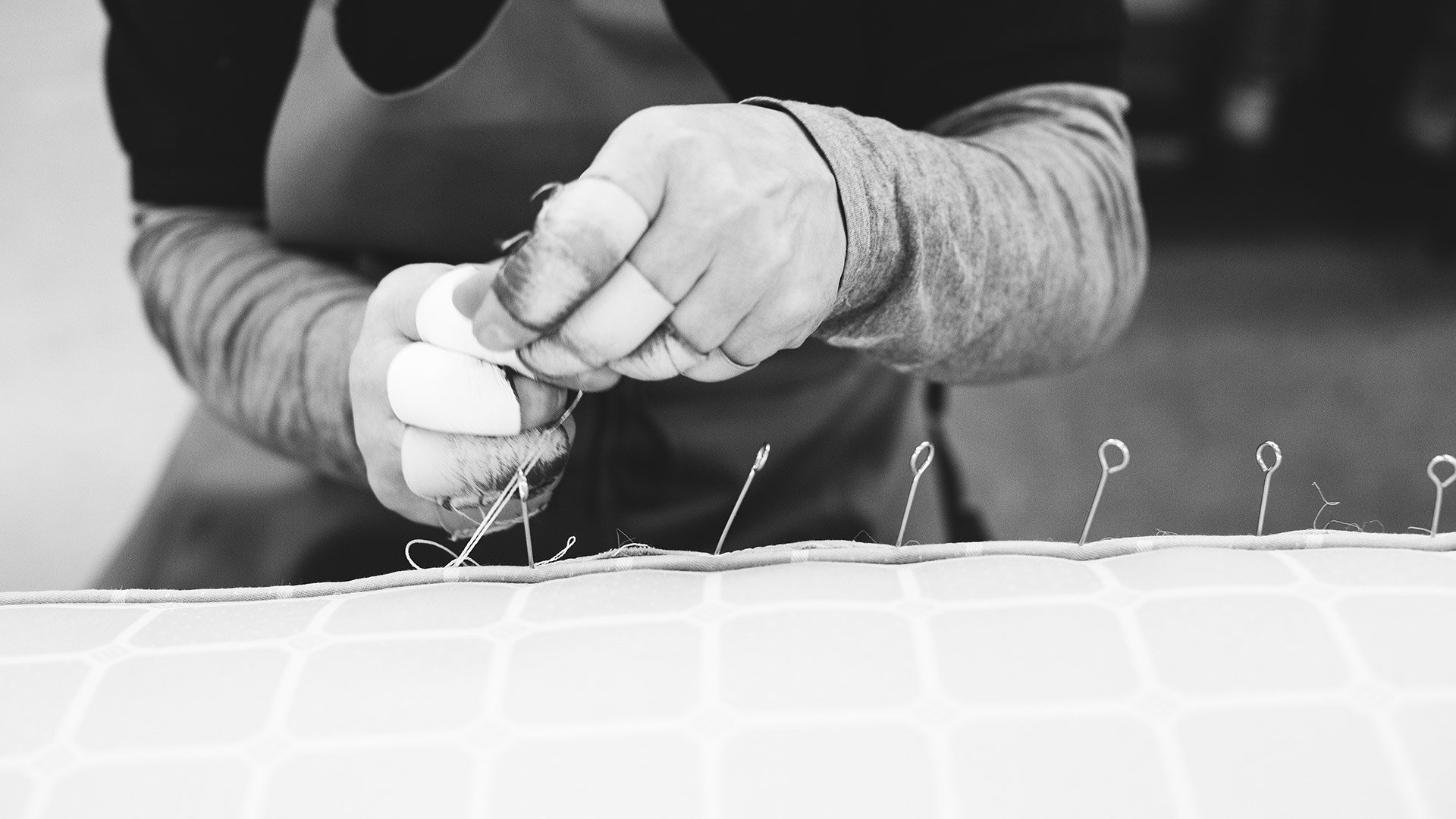 Black and white image of a Savoir craftsman side stitching a mattress at our London Bedworks