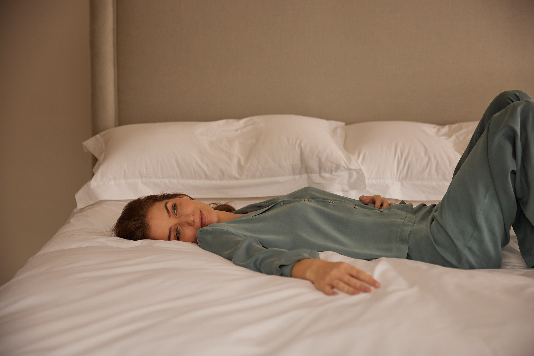 A woman resting on a Savoir bed dressed in all-white bed linen