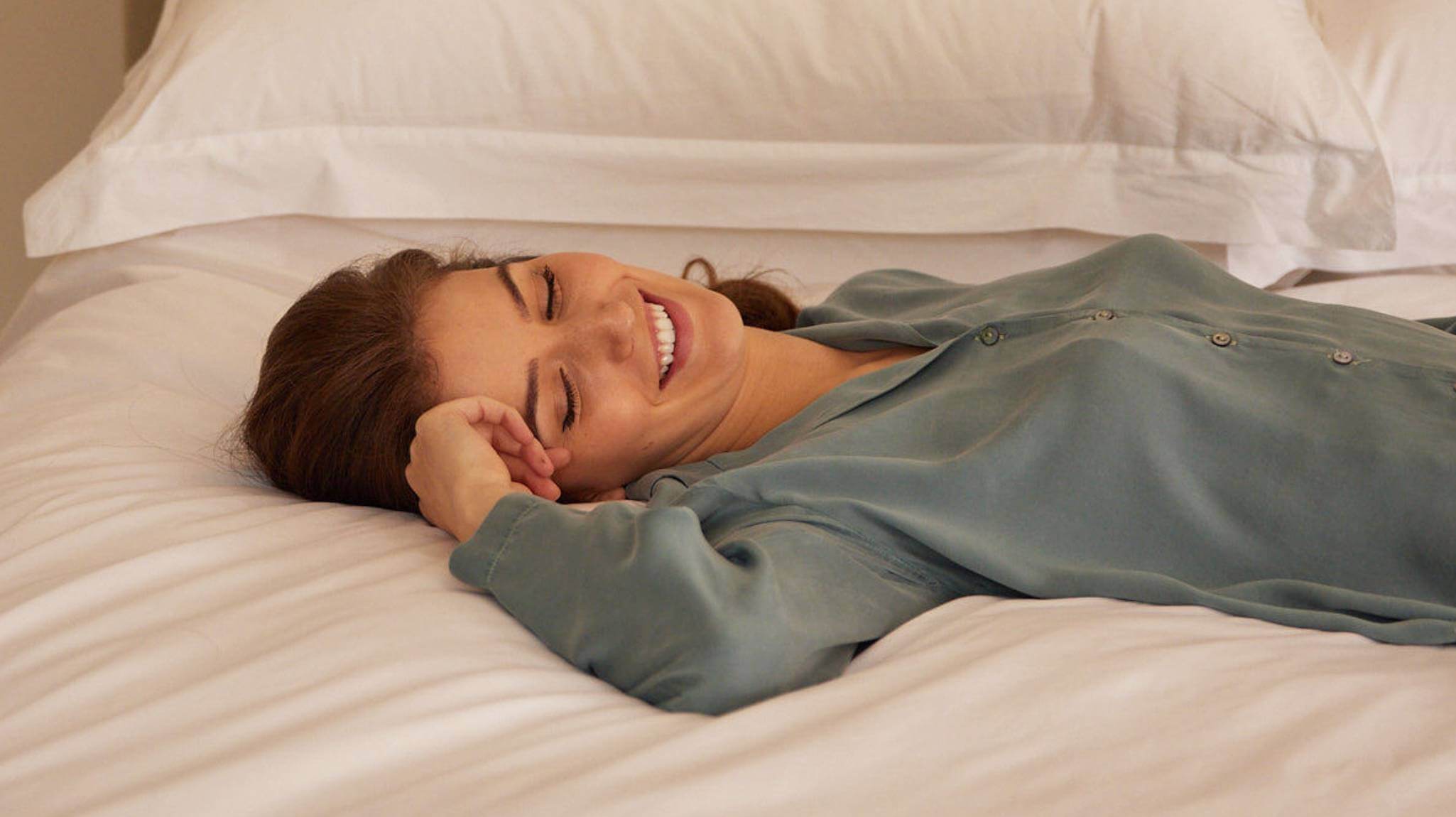 Woman resting on a Savoir bed wearing cotton pyjamas, with the bed dressed in crisp white bed linen