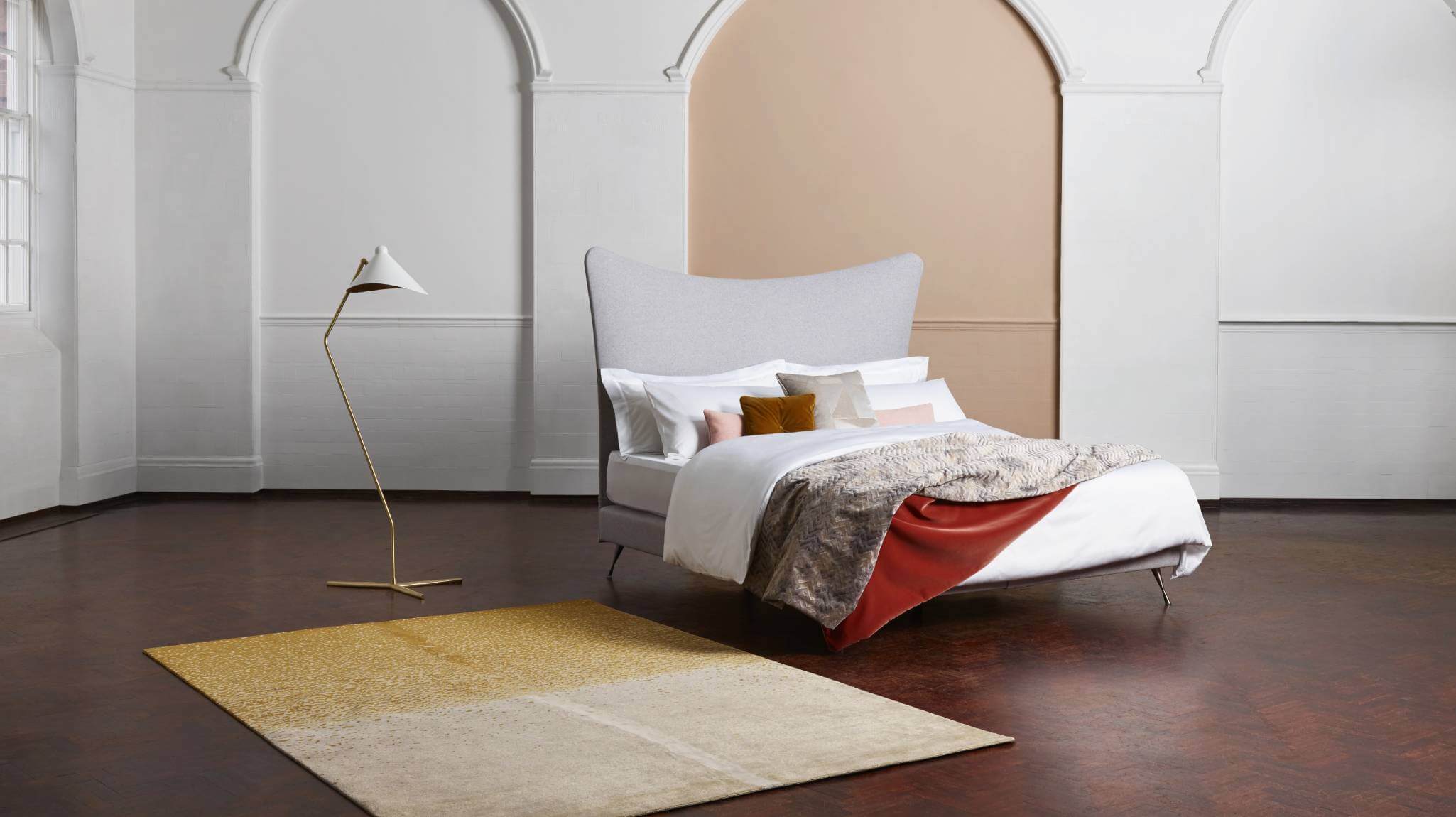 A bed with a dynamic headboard upholstered in calming grey fabric, photographed against a white wall.