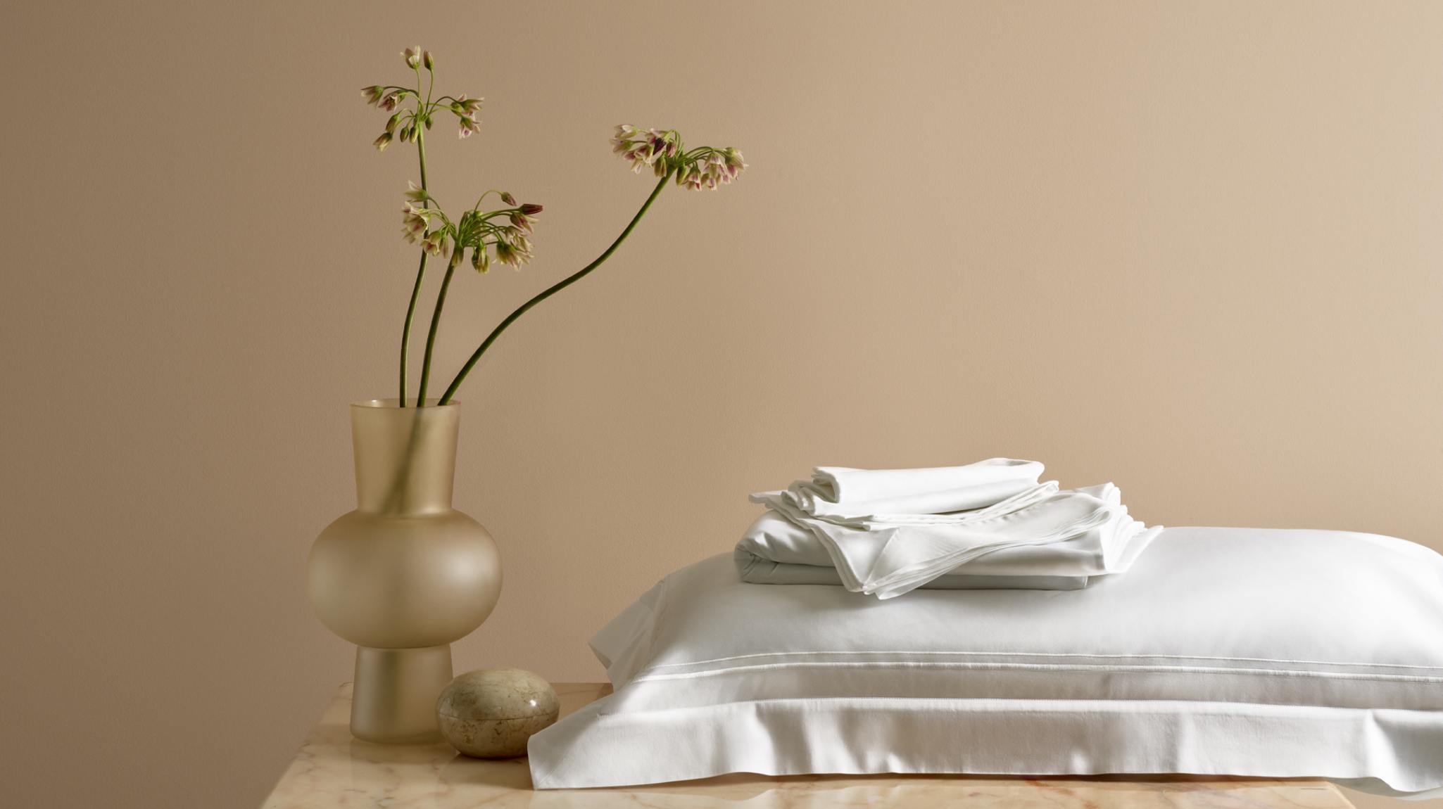 Savoir sateen bed sheets folded together and folded against a pale beige background