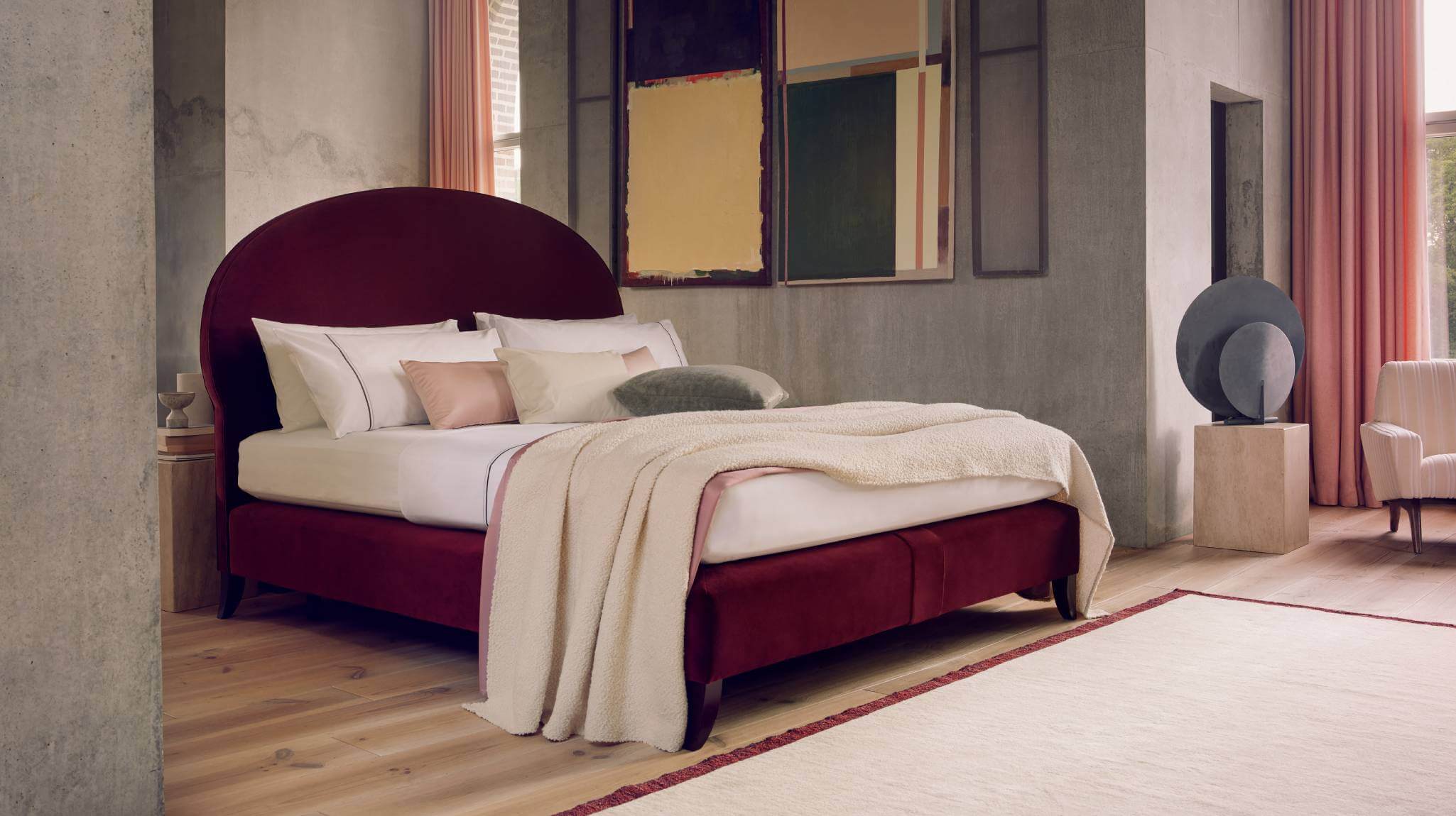 Our Elly bed upholstered in deep, red velvet, photographed against brutalist features of the Upper Farm House in United Kindgom