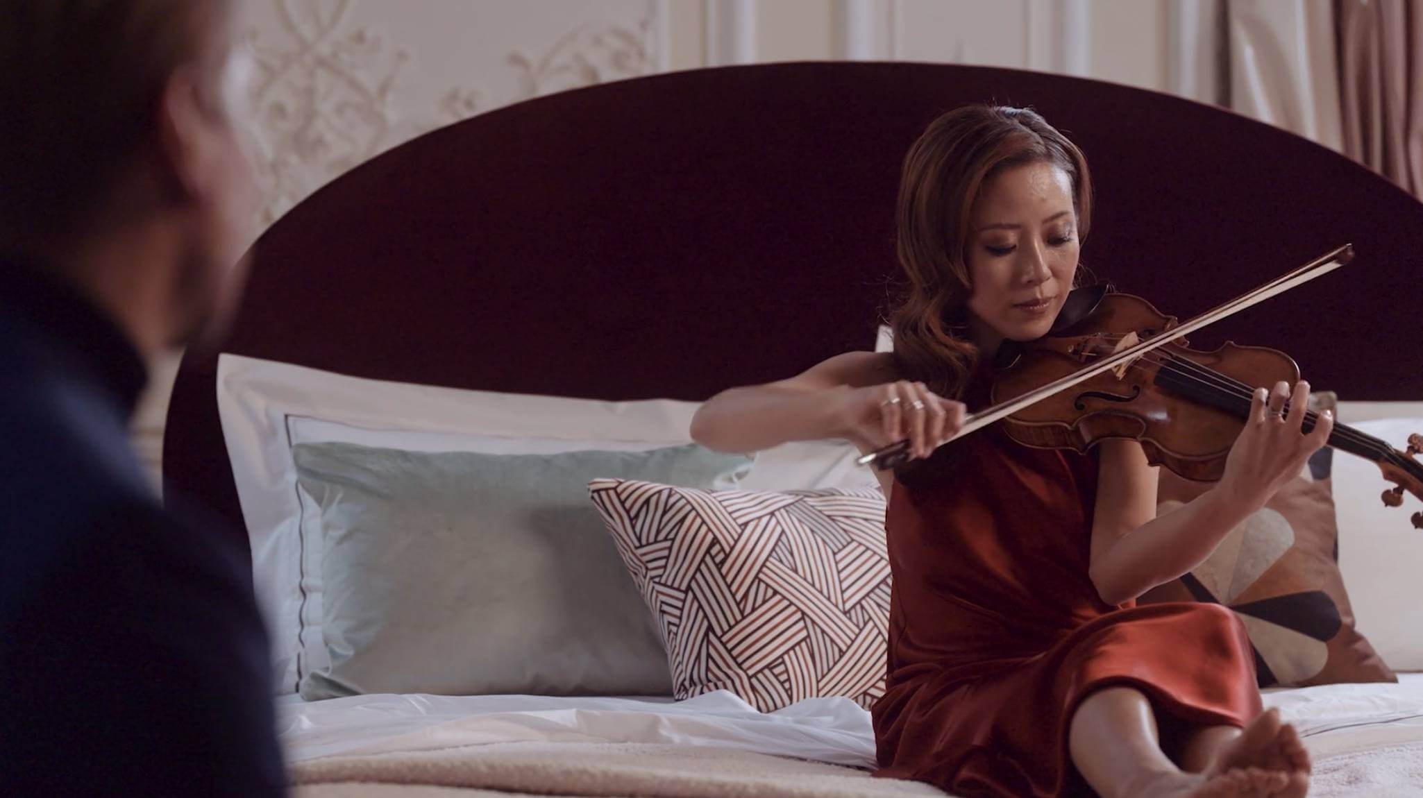 Image of violinist Elly Suh and her husband Florian Leonhard on a Savoir bed upholstered in rich, red velvet