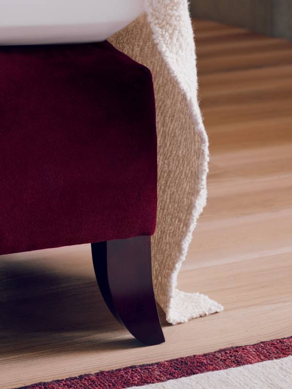 A close-up image of the Elly bed showcasing the Holly leg in Rosewood and the deep ruby upholstery