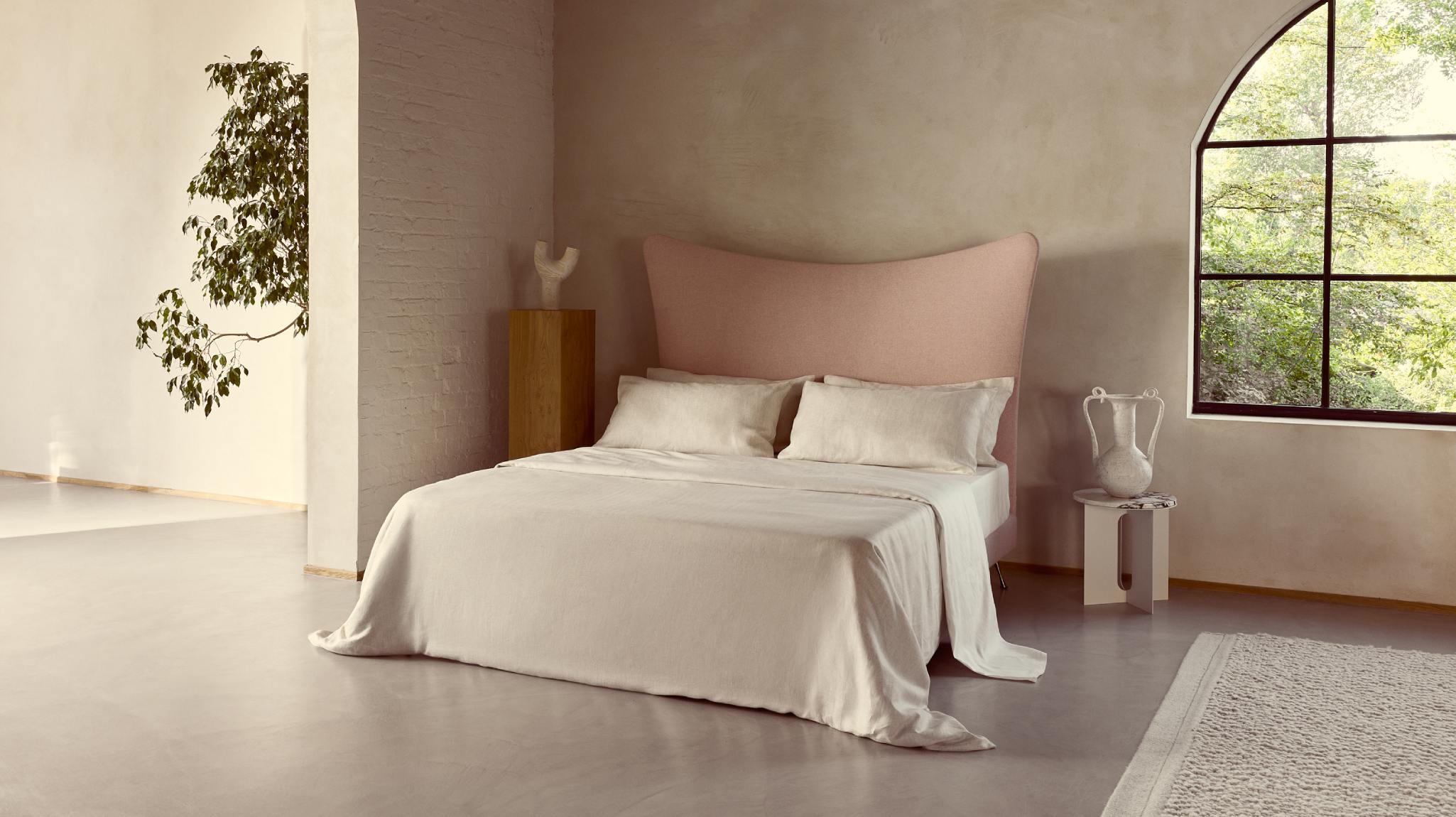 Softly curved Amelia bed upholstered in directionless Kvadrat wool in pink, dressed in calming herringbone bedding.