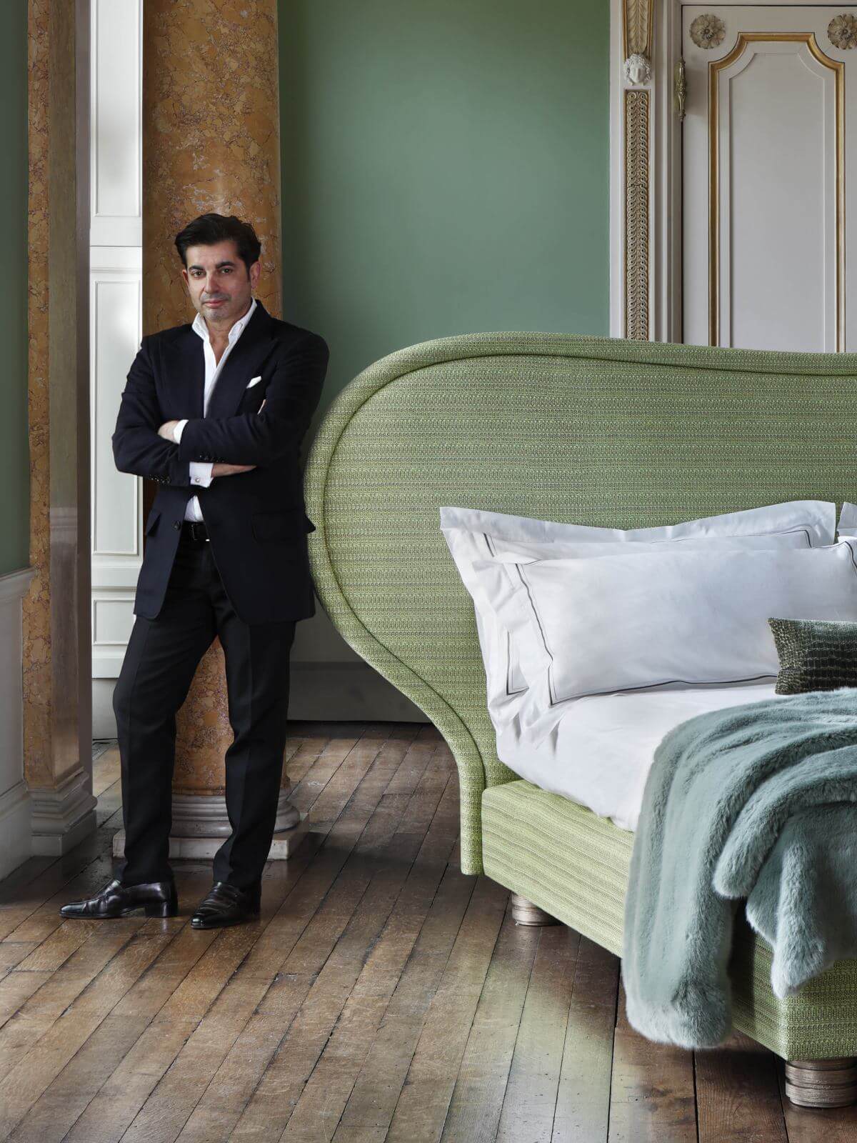 Designer Francis Sultana standing next to his design for Savoir, the Louis Bed, featuring bright green tweed upholstery and a dynamic, curved headboard.