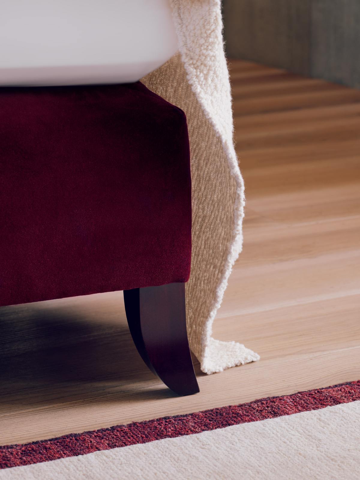 Detail image of the Elly bed, upholstered in rich, red velvet with ebony wooden legs.