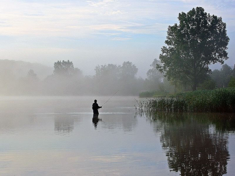 Image of a person fishing at sunrise in a peaceful lake