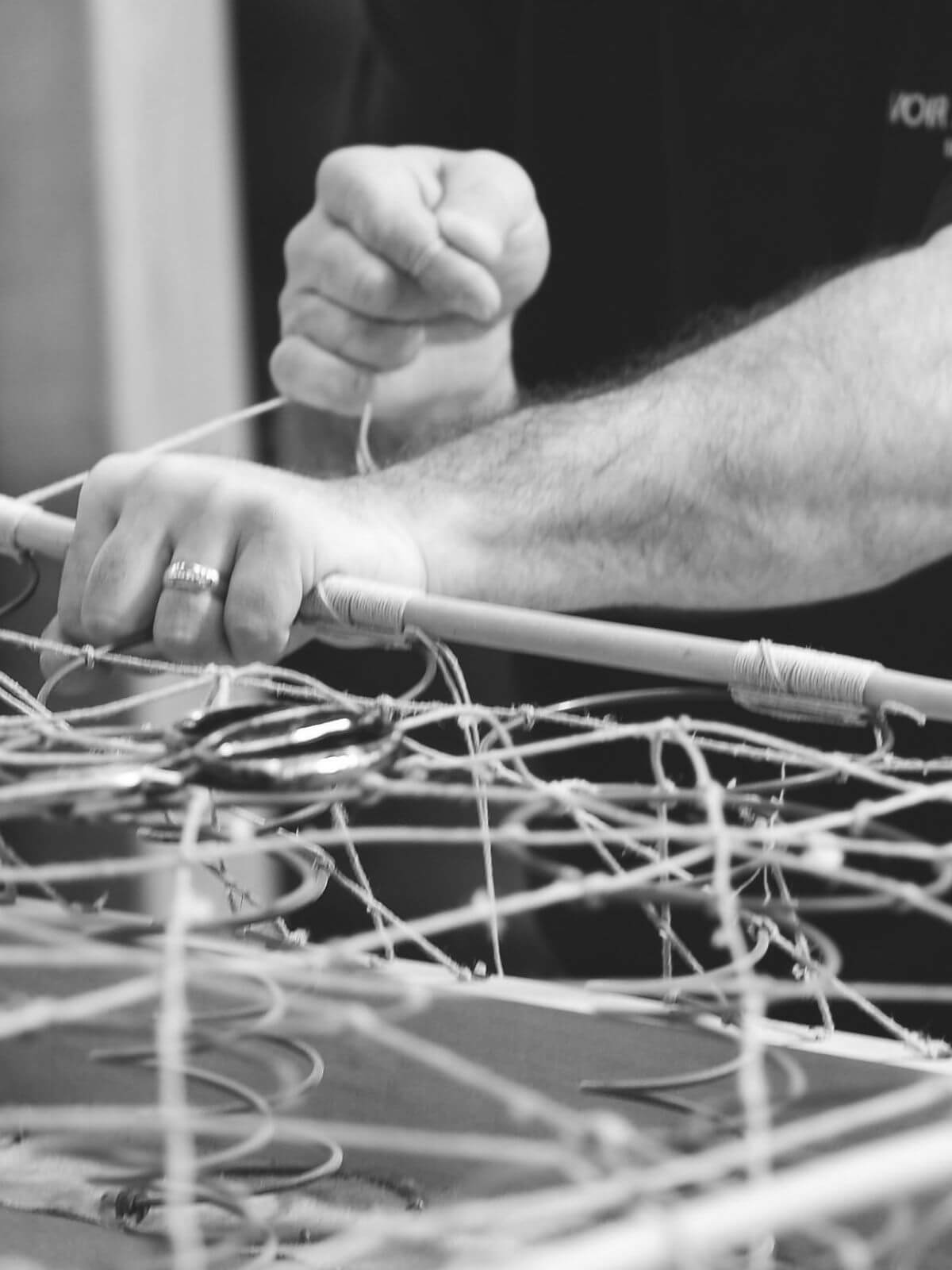 A black and white image showing a Savoir craftsman star-lashing the springs into the custom-made base