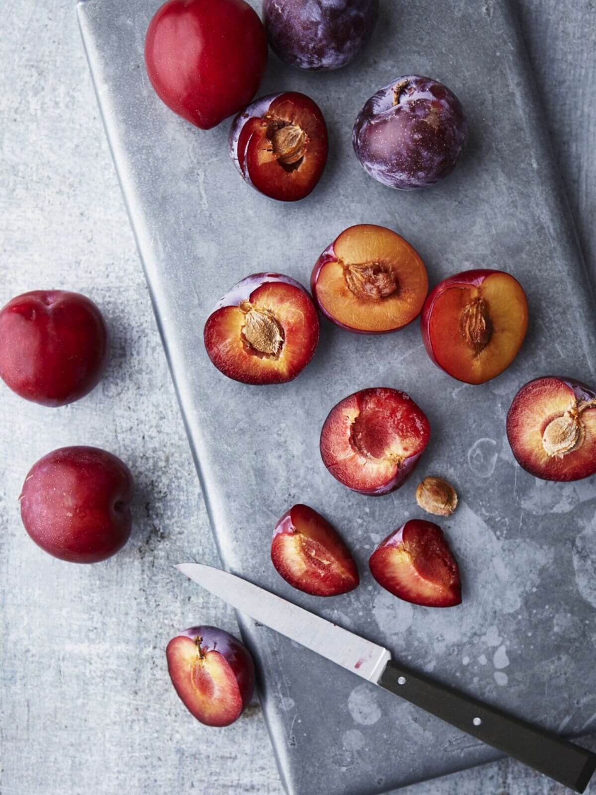 An image of cut-up fresh plums on a grey concrete table