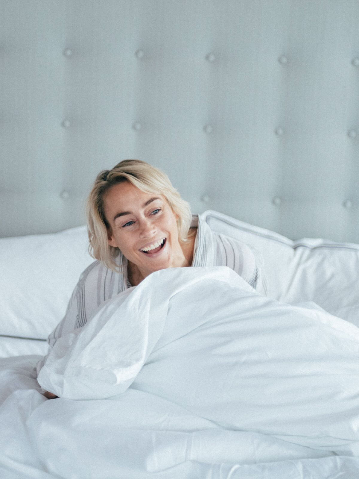 Image of a woman enjoying her morning on a comfortable bed, dressed in white bed linen