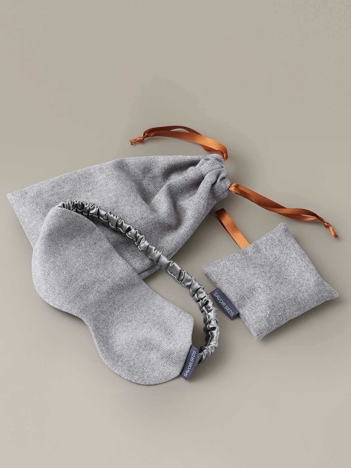 Image of the Savoir sleep kit in grey wool, with a silk eye mask, a lavender bag and a luxurious travel pouch with orange ribbon