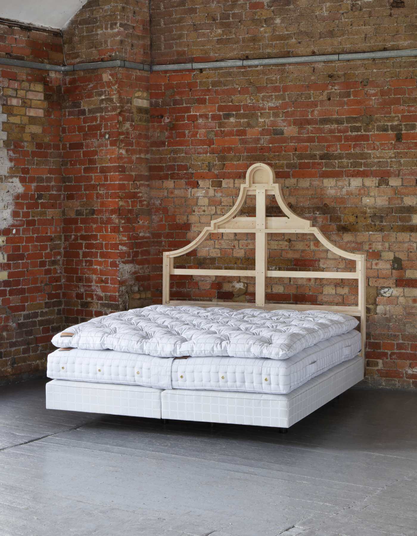 Image of a naked Savoir bed featuring the topper, mattress and box spring all upholstered in the signature Trellis ticking fabric photographed against a brick wall