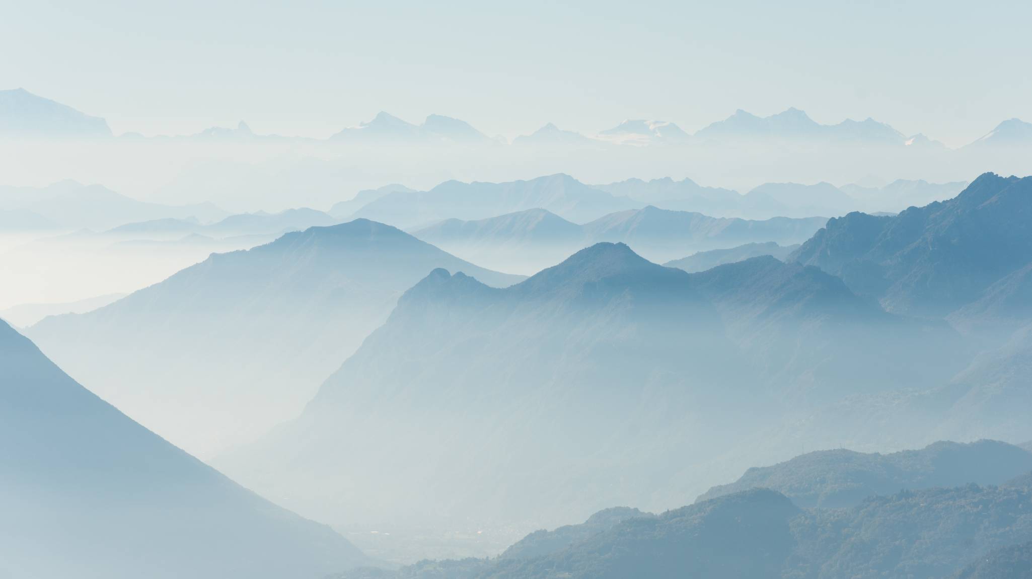 Image of clouds, mountains and trees in a distance, covered in light blue mist