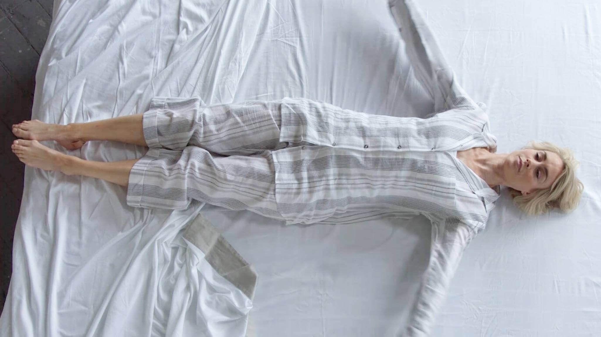 A woman lying down on a bed sideways, wearing striped cotton pyjamas.