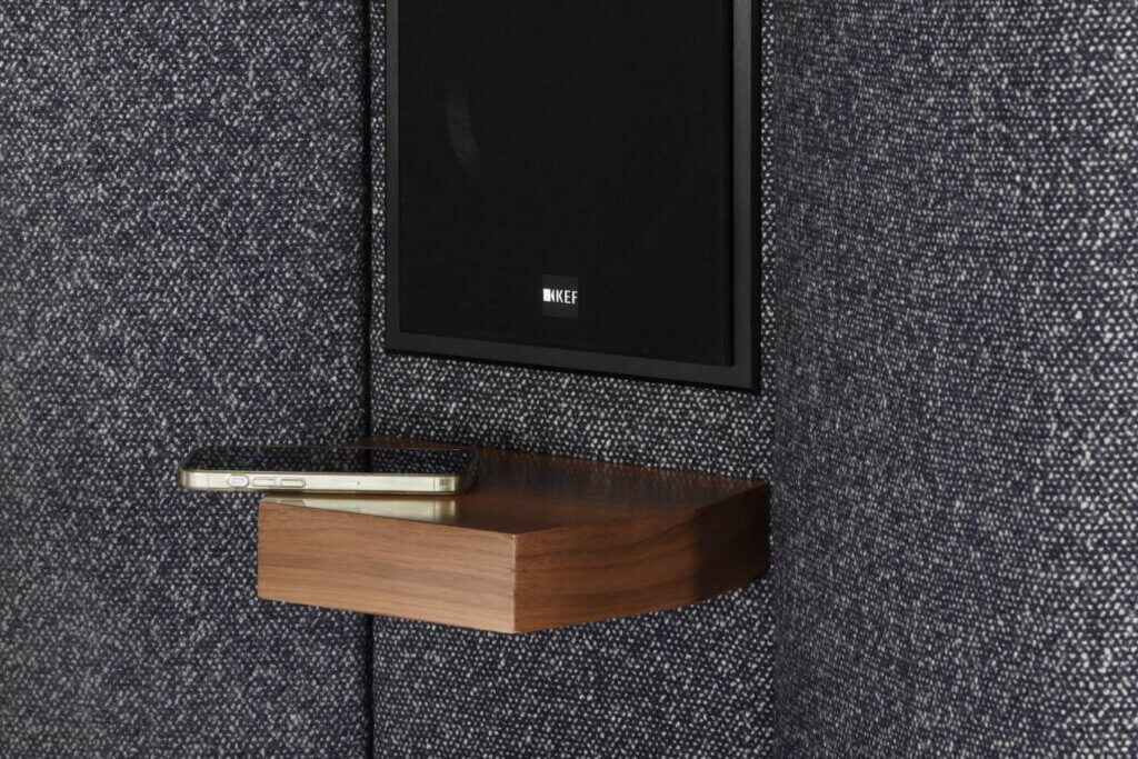 A close up image of the speakers integrated into our Seventy Five bed, featuring an American Walnut side table with a phone resting on it.