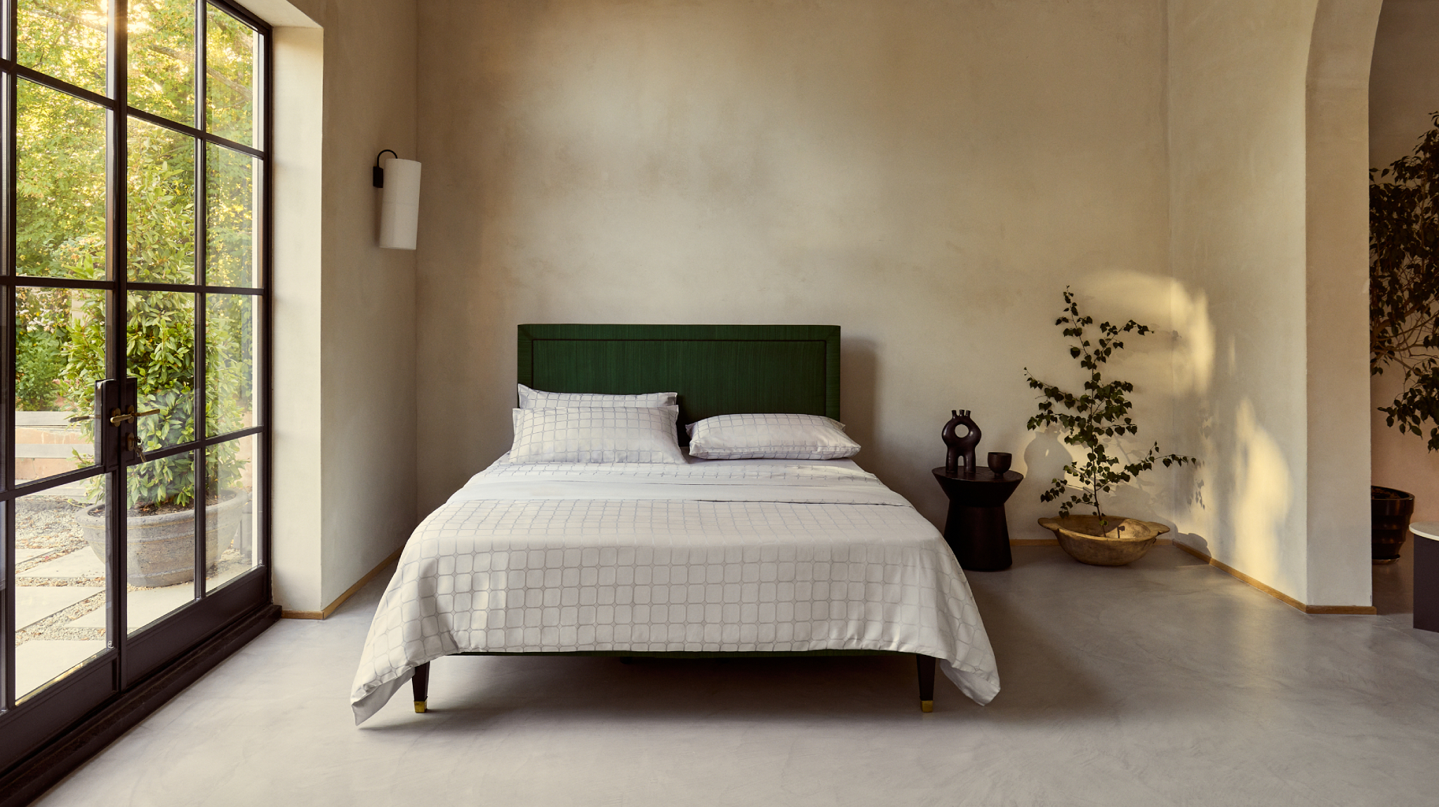 A bright green bed photographed against a serene setting, dressed in silver patterned bed linen.