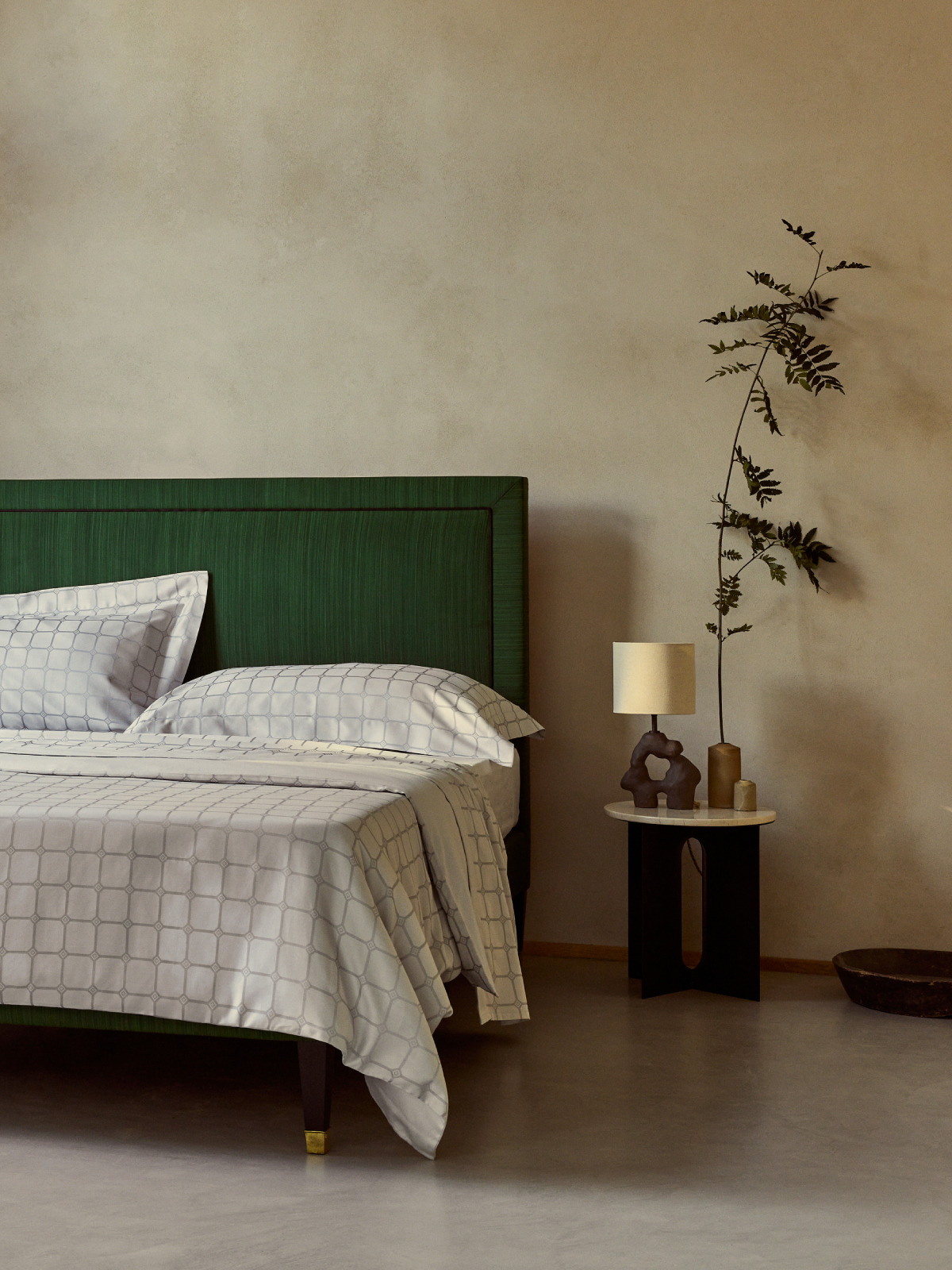 Detailed image of the Trellis patterned bed linen in silver, photographed on a bright green bed against a serene setting.