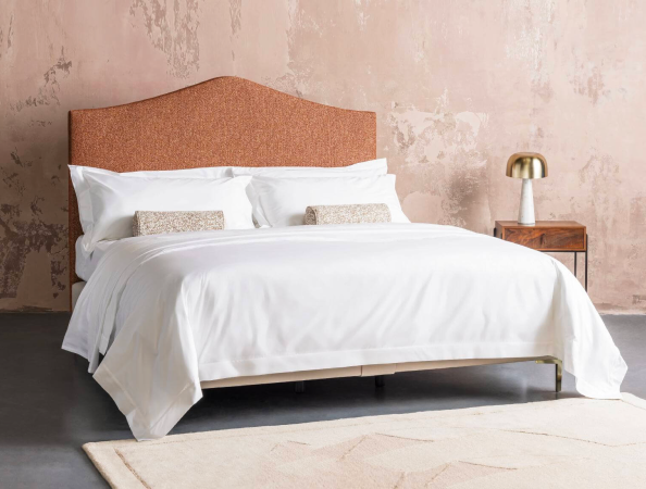 No5 Savoir bed featuring a curved headboard, upholstered in coral tweed against a pale pink rustic background.