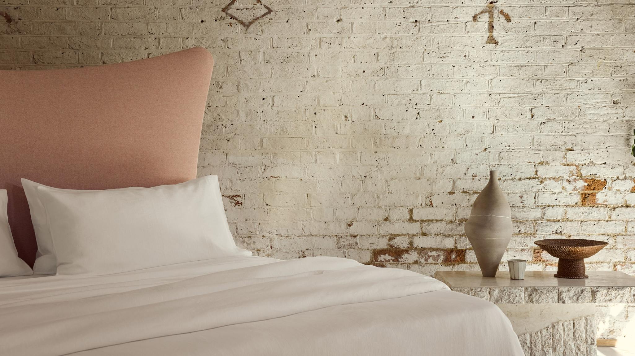 Luxurious organic linen sheets photographed on curved pink headboard against a calming setting